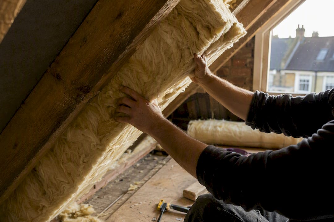Hands installing loft insulation in attic