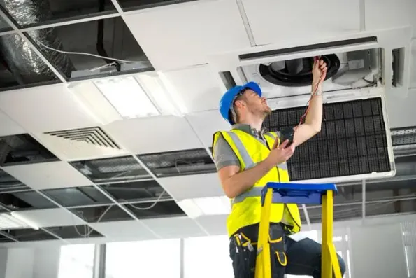 Worker repairing ceiling air conditioning unit.