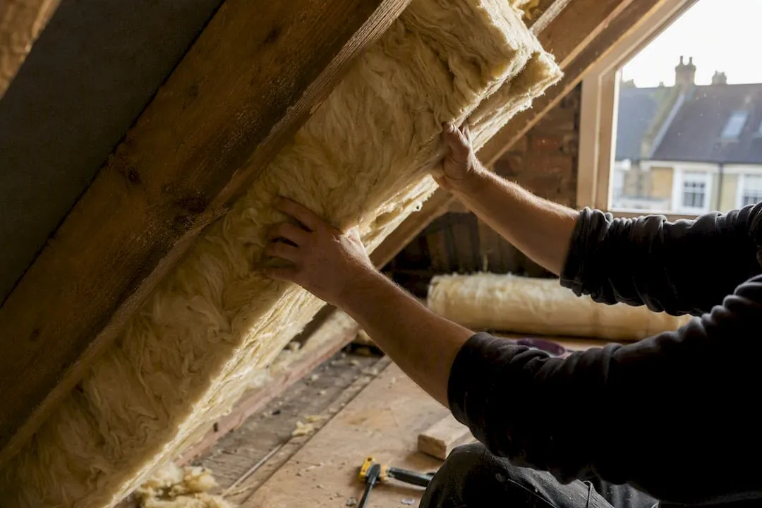 Hands installing loft insulation in attic
