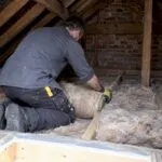 Installer laying loft insulation between joists